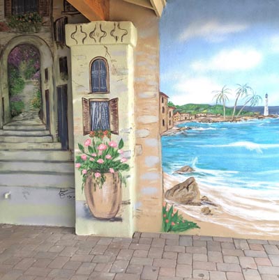 Trompe l'oeil mural of a Mediterranean street leading toward a sparkling blue sea.
