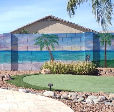 Tropical sunset beach mural with palm trees painted on a backyard block wall.