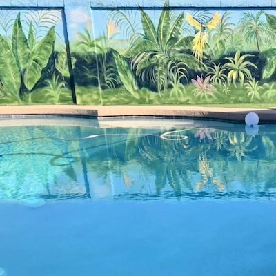 Lush tropical garden mural with palms and plants surrounding a swimming pool.